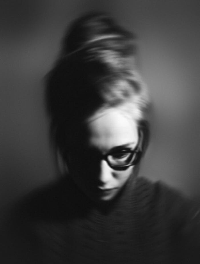 Grayscale portrait of a woman with glasses, exhibiting a pensive mood in studio lighting.